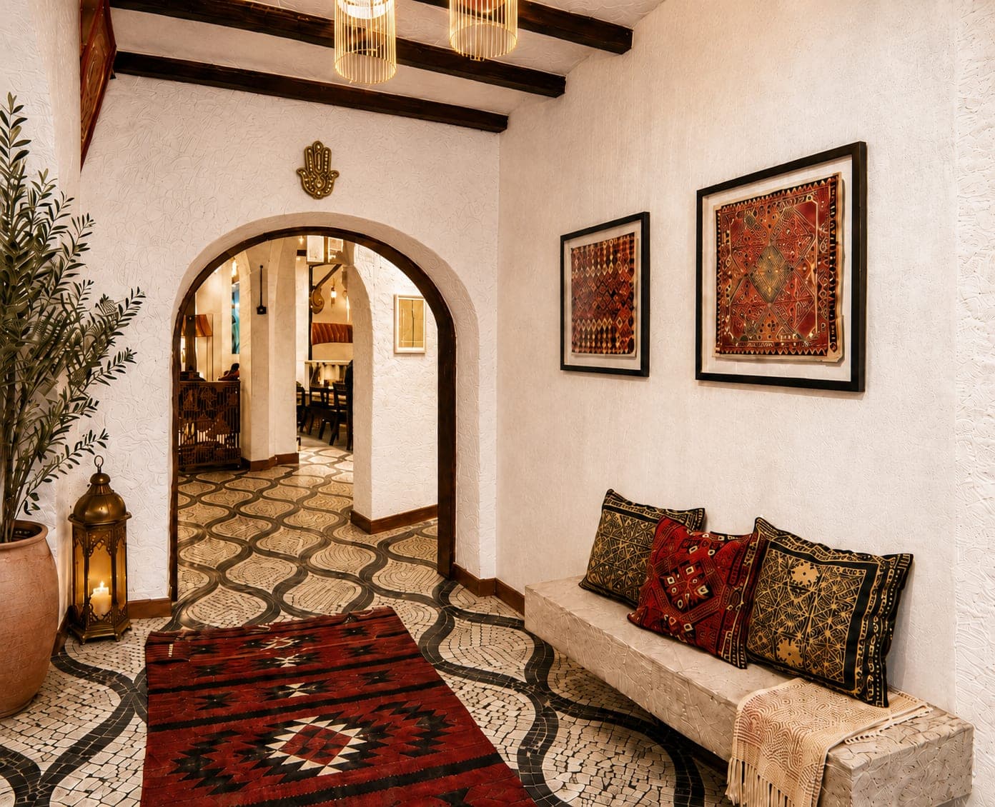 A House entrance hall — an arched doorway, framed tatreez, and a bench dressed in embroidered cushions.