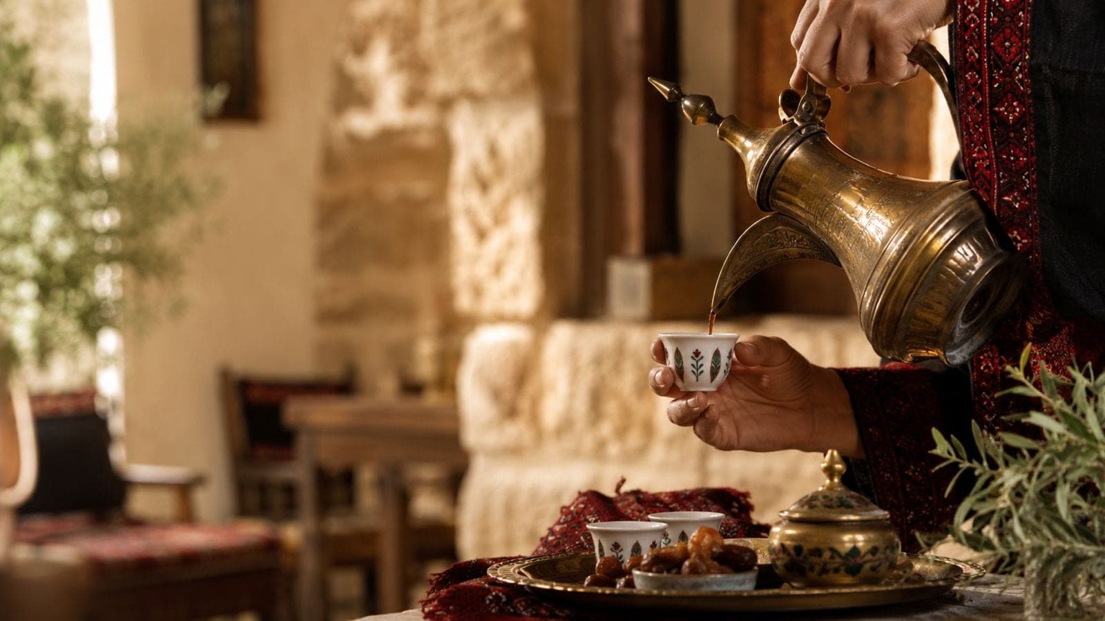 Arabic coffee being poured from a brass dallah into a small cup.