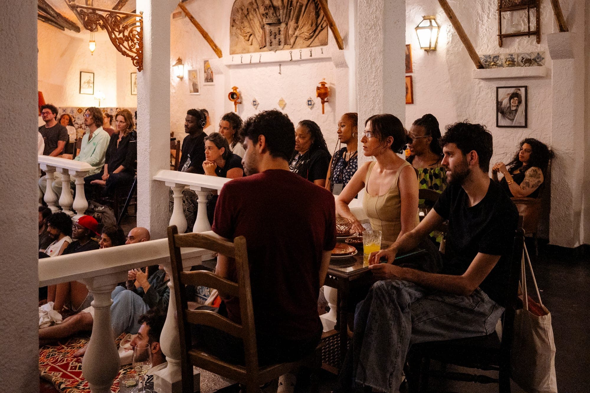 The café room by day — guests at wooden tables under the arches, listening in.