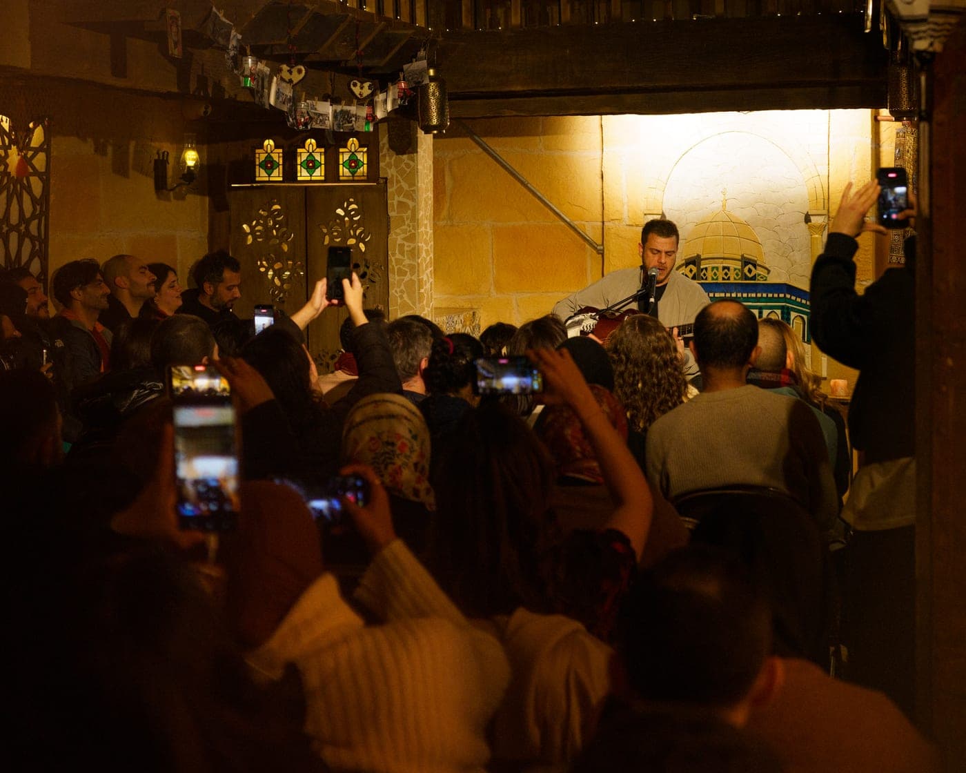 A packed audience filming a candlelit night of live music.
