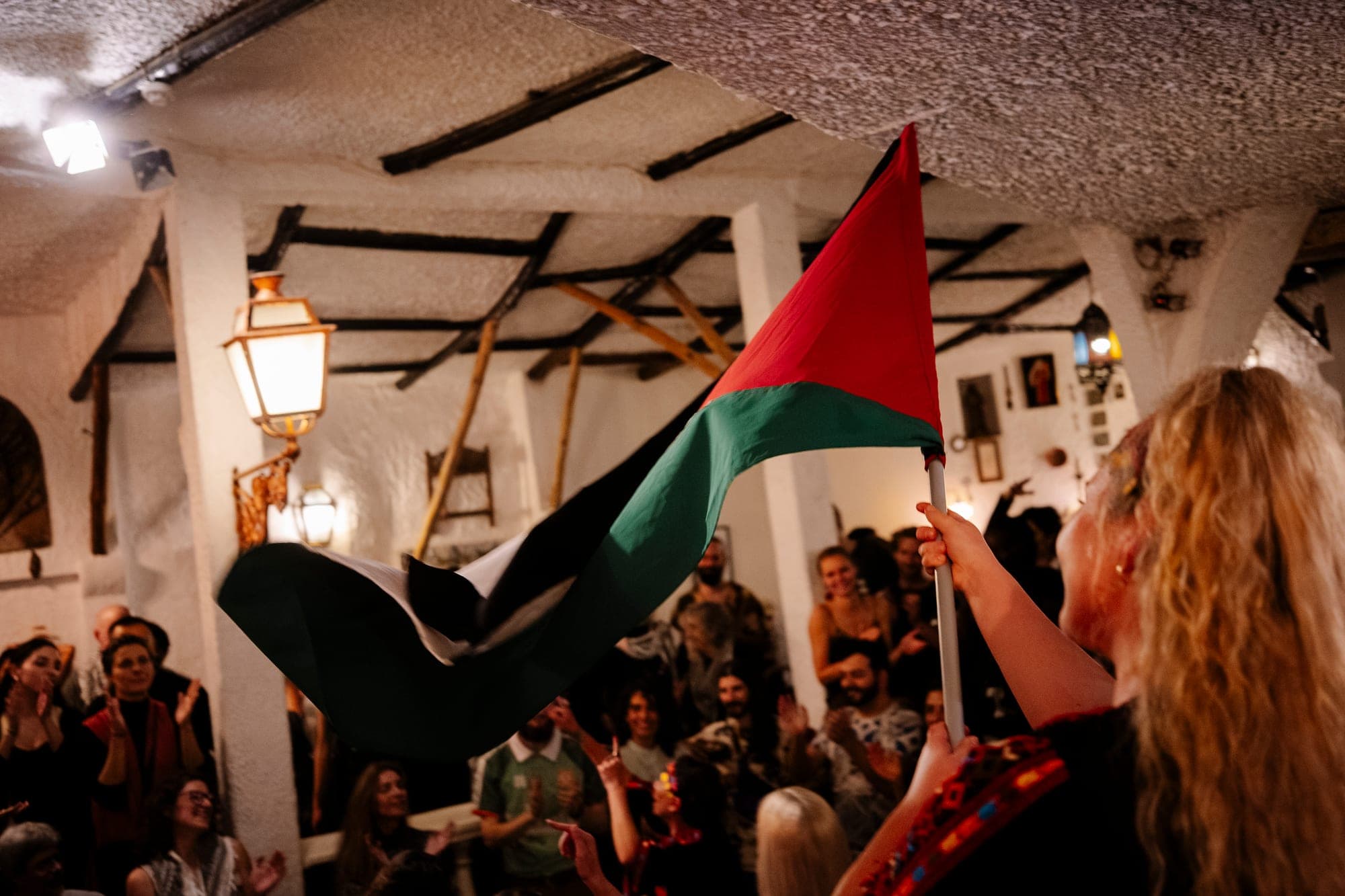 A woman waving a Palestinian flag as a House gathering claps her on.