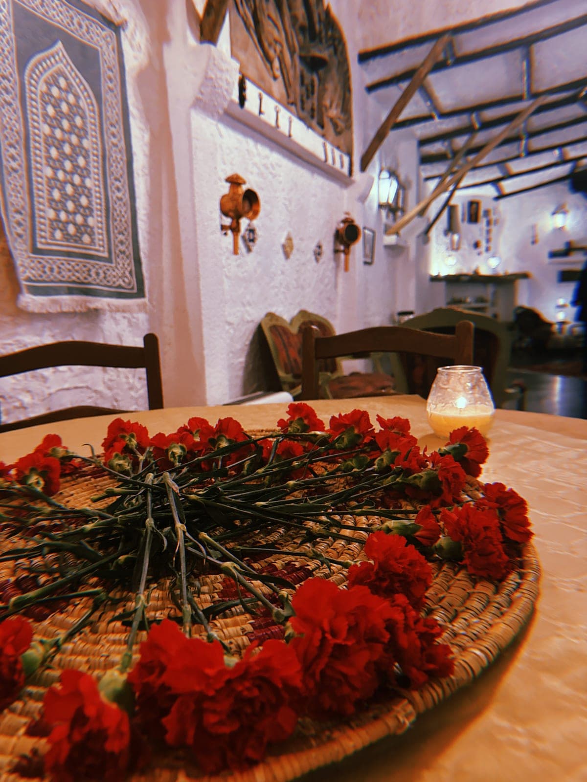 A candlelit café table set with red carnations.